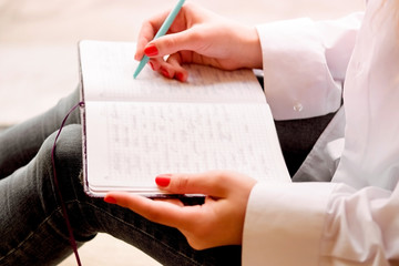 Beautiful sexy girl sits on a windowsill with a notebook and thinks. Details close up. A lonely...