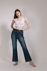 Girl in jeans and barefoot posing on a white background