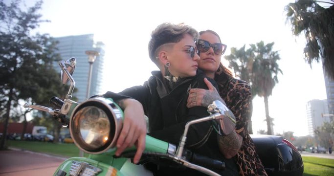 Lesbian couple sitting together on motorcycle in city streets