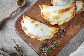 Traditional Argentine hot food made with meat and onion called empanada on wooden board and white background.