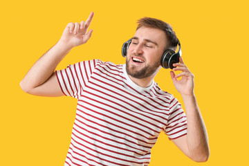 Handsome young man dancing and listening to music against color background