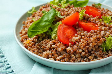 Plate with tasty buckwheat porridge and vegetables on table, closeup