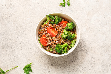 Bowl of tasty buckwheat porridge and vegetables on grey background