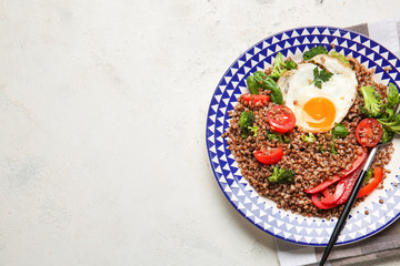 Plate with tasty buckwheat porridge, egg and vegetables on white background