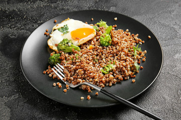 Plate with tasty buckwheat porridge, egg and broccoli on dark background