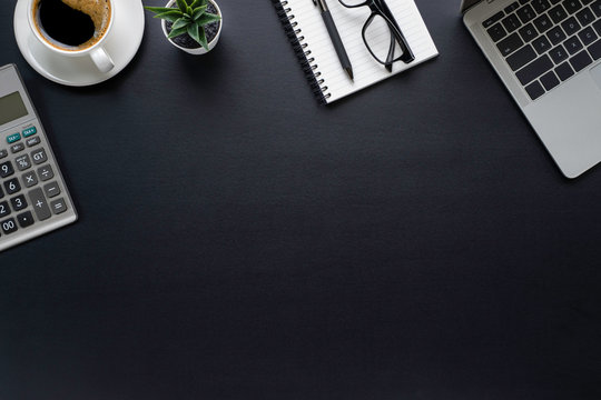 Workspace in office with black table. Top view from above of laptop with notepad and coffee. Desk for modern creative work of designer. Flat lay with blank copy space. Business and finance concept.