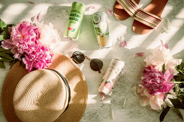 Obraz na płótnie Canvas Summer flatlay. Sunglasses, summer hat, flip flops, peony flowers and refreshing sparkling water in cans. Bright and colorful. Direct sunlight. Harsh sunlight. Flat lay on white background.Summer time