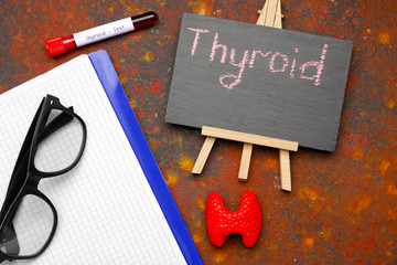 Chalkboard with text THYROID, notebook, eyeglasses and blood sample on color background