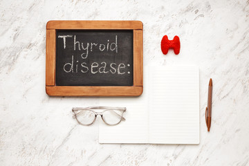 Chalkboard with text THYROID DISEASE and notebook on white background