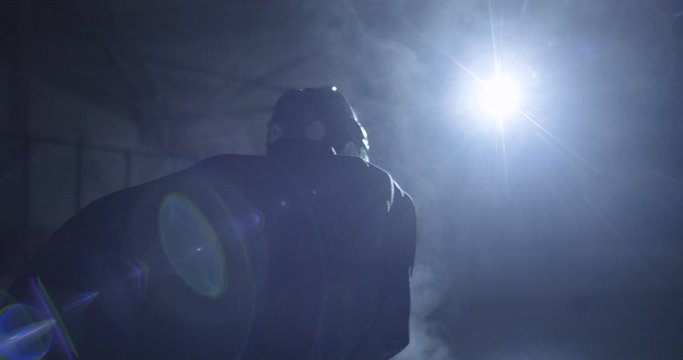 Camera round shot of Caucasian handsome male hockey player in uniform and helmet getting ready to hit on icy arena during game. Dark silhouette of sportsman on ice.