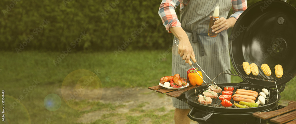 Wall mural man having picnic and cooking food on barbecue grill outdoors, closeup with space for text. banner d