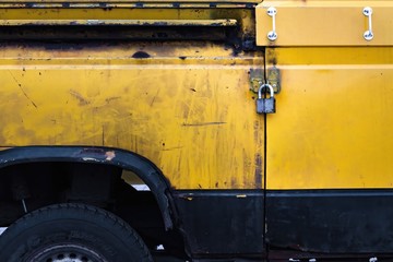 
An old minivan with a textured metal rusty yellow body and with a padlocked door. Apparently the...
