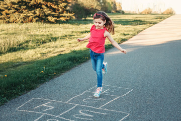 Cute adorable little young child girl playing hopscotch outdoors. Funny activity game for kids on playground outside. Summer backyard street sport for children. Happy childhood lifestyle. - 353009482