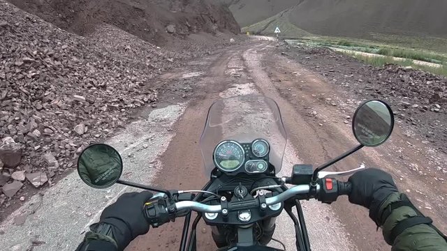 A biker slow driving on extremely dangerous mountain mud road, passing through a rocky, landslide region in Himalayas. This is a point of view shot.