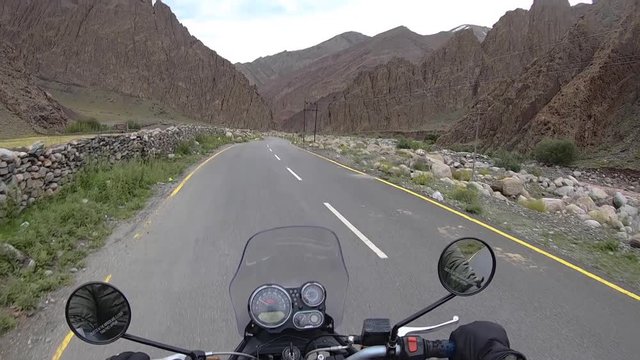 A biker riding his vehicle on a well built road through a beautiful Himalayan valley with steep barren mountains nearby. Shot on a cloudy day from biker&rsquo;s point of view.