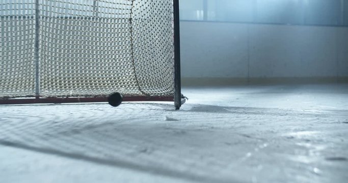 Close up of puck hitting with club and scoring goal. Camera following hockey player feet in skaters sliding fast on ice. Sportsman skating on icy arena and putting disc in gate with stick.
