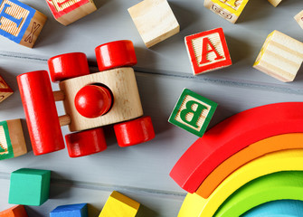 Close up Multicolored wooden cubes with letters, car, rainbow arc on gray background. Set of toys for studying alphabet. Education, back to school concept. Top view, copy space