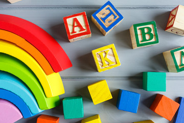 Close up Multicolored wooden cubes with letters, pencils, rainbow arc on gray background. Set of toys for studying alphabet. Education, back to school concept. Top view, copy space