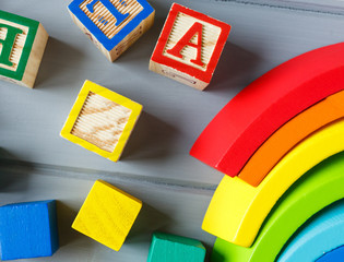 Close up Multicolored wooden cubes with letters, pencils, rainbow arc on gray background. Set of toys for studying alphabet. Education, back to school concept. Top view, copy space