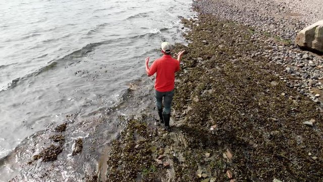 Asian male walks down beach fly fishing in Puget sound wearing a red shit.