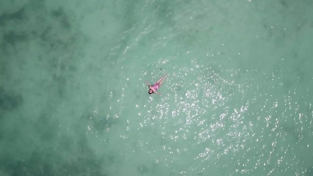 A directly above view of a young woman swims in shallow turquoise water near the shore of Saona Island, in the Dominican Republic