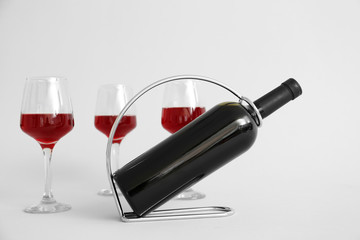 Holder with bottle and glasses of wine on grey background