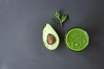 mint, half avocado and glass with green smoothie on a gray background. copyspace. top view