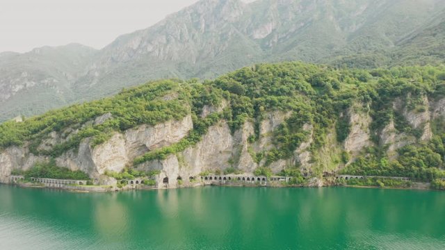 Aerial shooting of approaching the tunnel in the mountain surrounded by green water of Como Lake, Lecco, Italy.