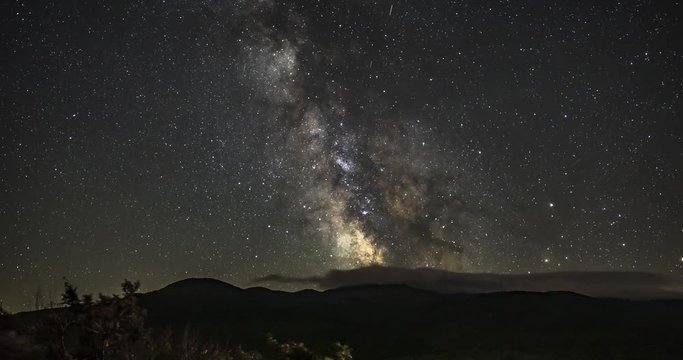 Night time-lapse of a starry sky and the milky way galaxy moving across the silhouette of mountains, while clouds circle around, in New Hampshire, USA. Includes 2 shots.