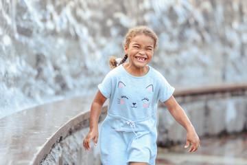 Happy beautiful girl running through the spray of water.
