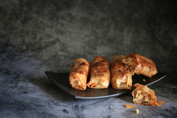 Deep-fried spring roll in black rectangle plate on a cement table