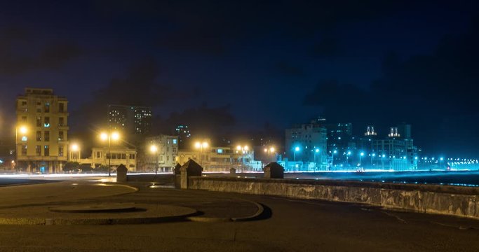 Evening to Night time-lapse along the El Malecon waterfront in Havana Cuba, with old apartment buildings in the background.