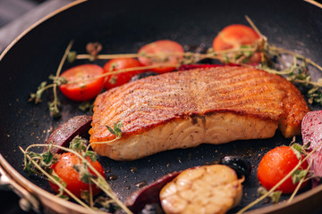 Tasty salmon fillet with herbs and cherry tomatoes in a pan.