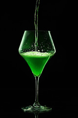 Green drink is poured into a glass. Black background.