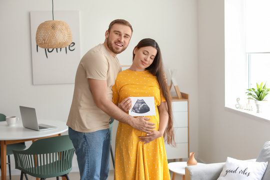 Beautiful pregnant woman with sonogram image and her husband at home