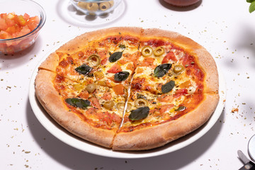 Pizza de massa pan tradicional de queijo mussarela com tomates picados, azeitonas verdes sem caroço e folha de manjericão sobre a mesa branca