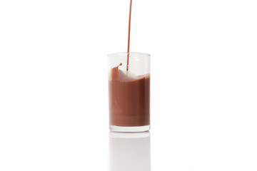 Almond chocolate milk in glass isolated on white background, pour action, falling, flowing and splashing motion. Dairy drink with creamy and sweet taste.