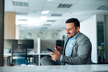 Naklejka na ściany i meble Charming smiling business man using smart phone at work, portrait.