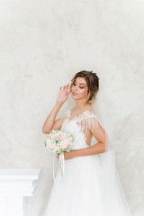Beautiful bride with a wedding bouquet in a beautiful white room, catalog of wedding dresses, beautiful bride waiting for the groom, portrait of the bride, single bride in a beautiful dress