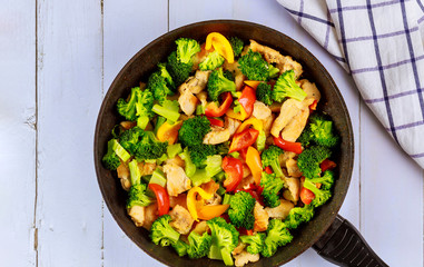 Healthy stir fry vegetables with chicken in pan on white surface.