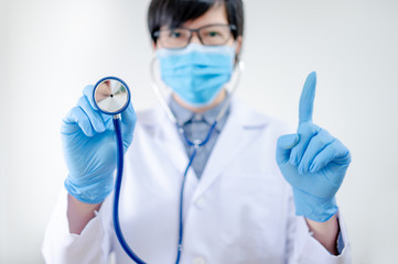 Healthcare and medical check up concept. Male Asian doctor holding stethoscope in hand. Physician man wearing surgical mask and gloves working in hospital clinic during Coronavirus (COVID-19) pandemic