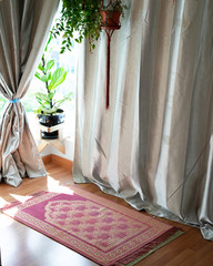Pray and worship area room at home for Muslim. Islamic prayer rug with hanging green plants with sunlights coming from the window. Beautiful Interior Design.