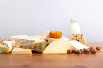 Heap of sliced and whole cheeses, bottle of milk and macadamia nuts on wooden table. Closeup shot. High protein food concept