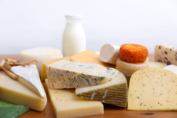Different sliced and whole cheeses and bottle of milk on wooden table. Closeup shot. High protein or dairy foods concept