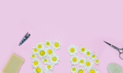 Creative concept of pedicure: feet laid out of chamomile, scissors, forceps, pumice. Personal care, spa.