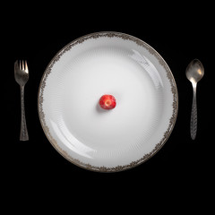 White plate on the black background served with a spoon right and a fork left. Strawberry without tail in the center.