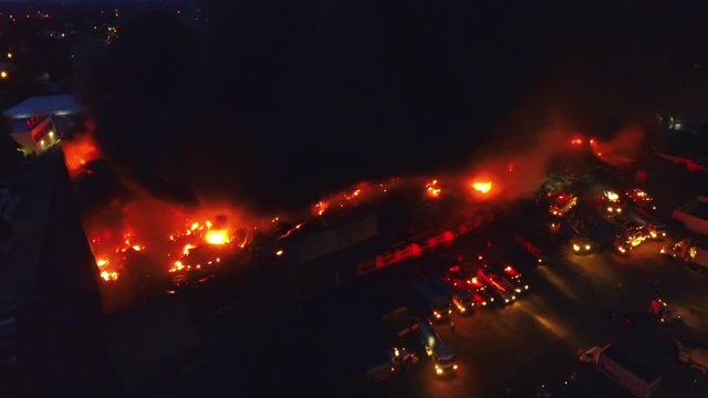 Aerial, tracking, drone shot overlooking firetrucks, vehicles and firemen trying to extinguish a building inflames, structure fire in Paris, France, Europe, during day time
