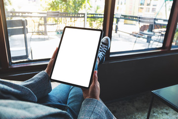 Mockup image of a woman holding black tablet pc with blank white desktop screen while sitting in...