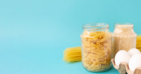 Noodles, rice, pasta in jars and eggs lie on a blue background. Raw food for cooking. There is a place for text