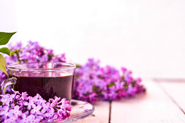 Obraz na płótnie Canvas Cup of tea with lilac flowers on a wooden white background. Mocap for postcards. Spring time. Vase with lilacs. Copy space for text. The concept of holidays and good morning wishes